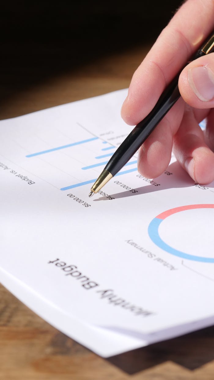 Close-up of hand analyzing data on a monthly budget document with graphs and charts.