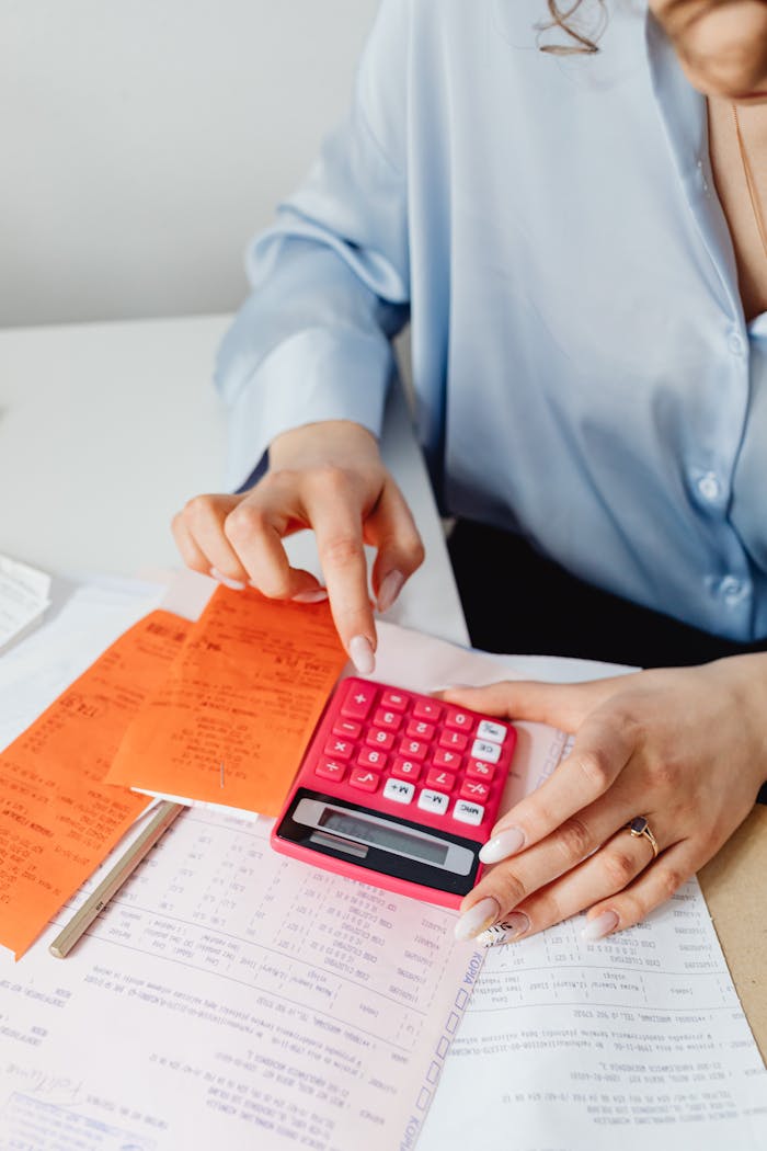 Person calculating finances with pink calculator and receipts, close-up view.